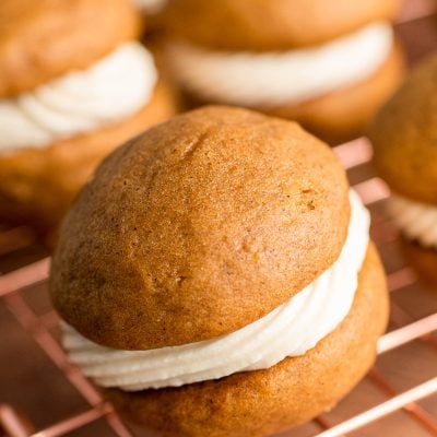 Close up photo of a pumpkin whoopie pie on a copper wire rack with more in the background.