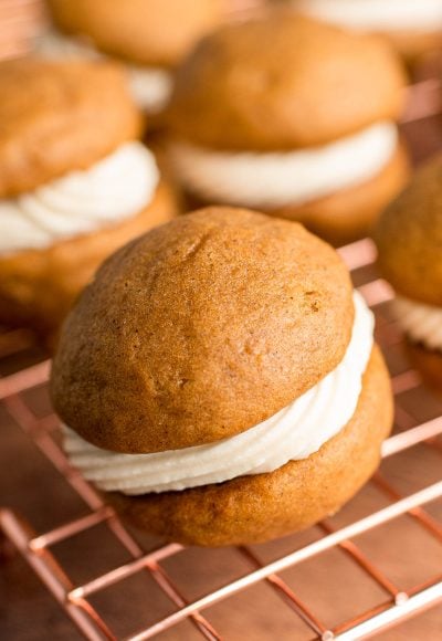 Close up photo of a pumpkin whoopie pie on a copper wire rack with more in the background.