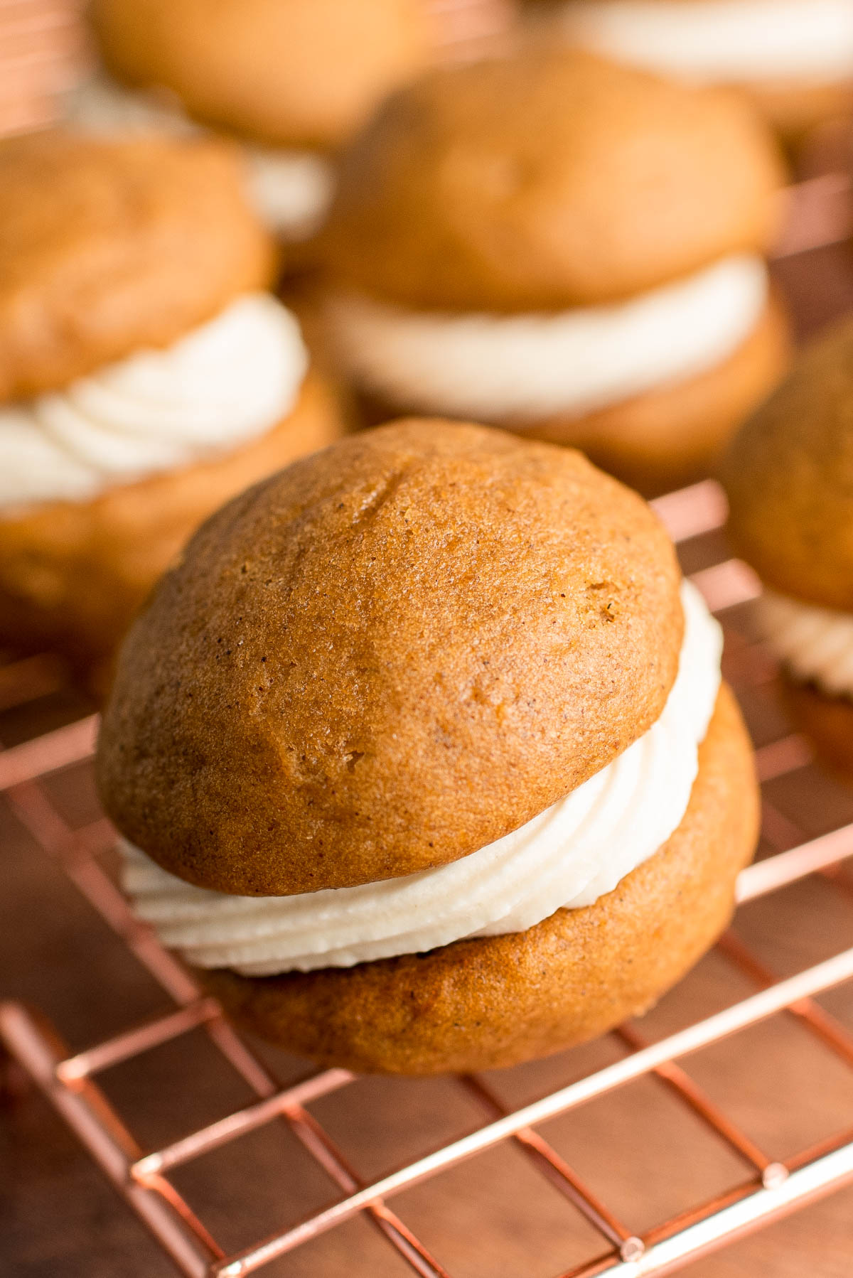 Close up photo of a pumpkin whoopie pie on a copper wire rack with more in the background.