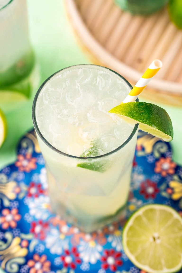 Close up photo of a ranch water cocktail on a colorful trivet with a white and yellow striped paper straw and lime wedges.