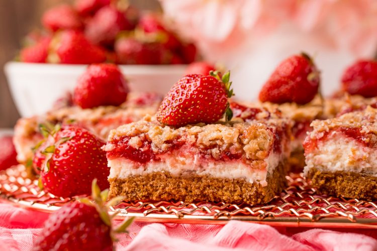 Close up photo of strawberry cheesecake bars on a copper wire rack on a pink napkin.