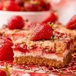 Close up photo of strawberry cheesecake bars on a copper wire rack on a pink napkin.