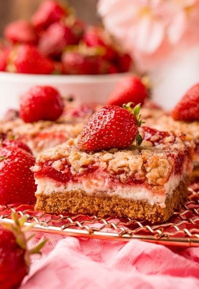 Close up photo of strawberry cheesecake bars on a copper wire rack on a pink napkin.