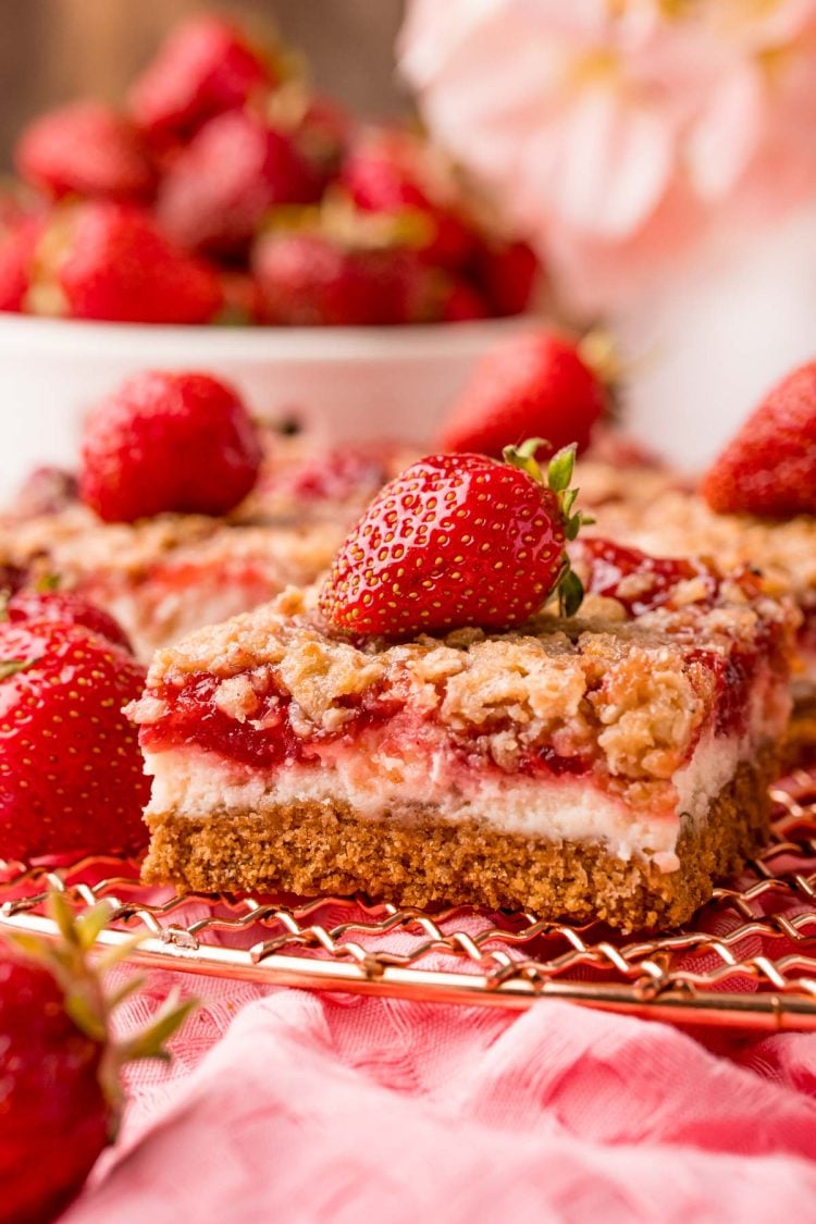 Close up photo of strawberry cheesecake bars on a copper wire rack on a pink napkin.