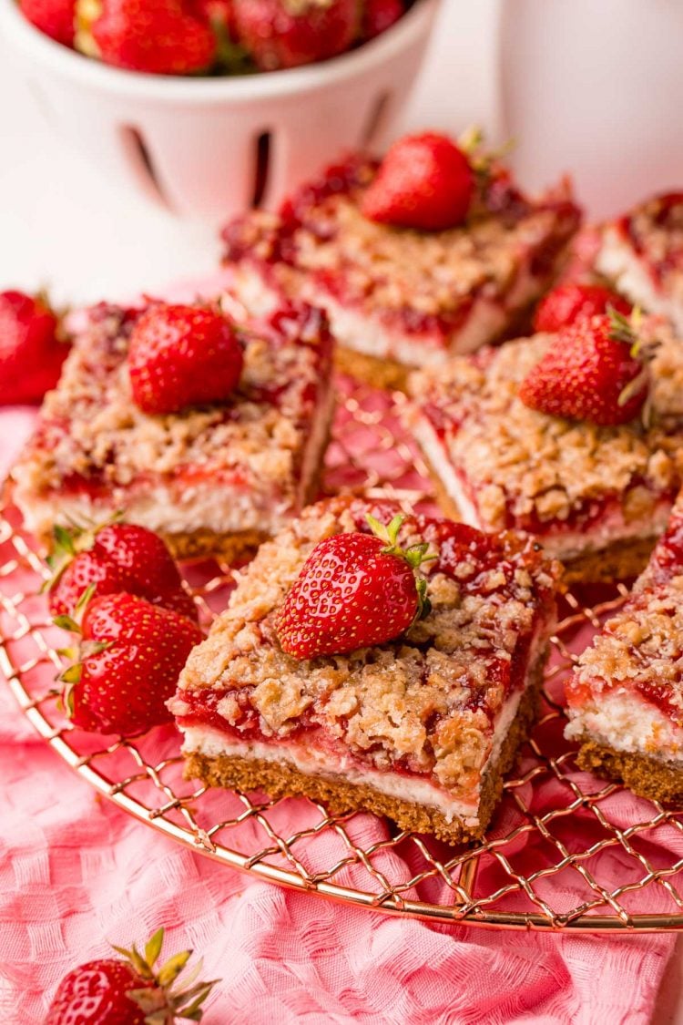 Close up photo of strawberry cheesecake bars on a wire rack on a pink napkin.