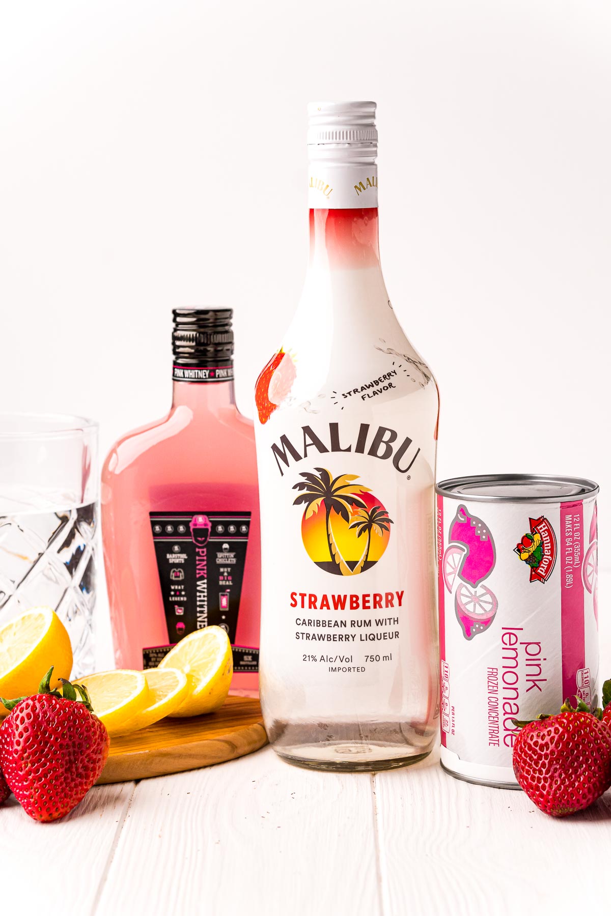 Ingredients to make strawberry lemonade cocktail on a white table.