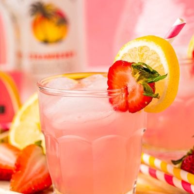 Close up photo of a small glass filled with a pink lemonade vodka cocktail on a rattan tray.