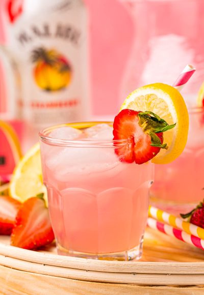 Close up photo of a small glass filled with a pink lemonade vodka cocktail on a rattan tray.