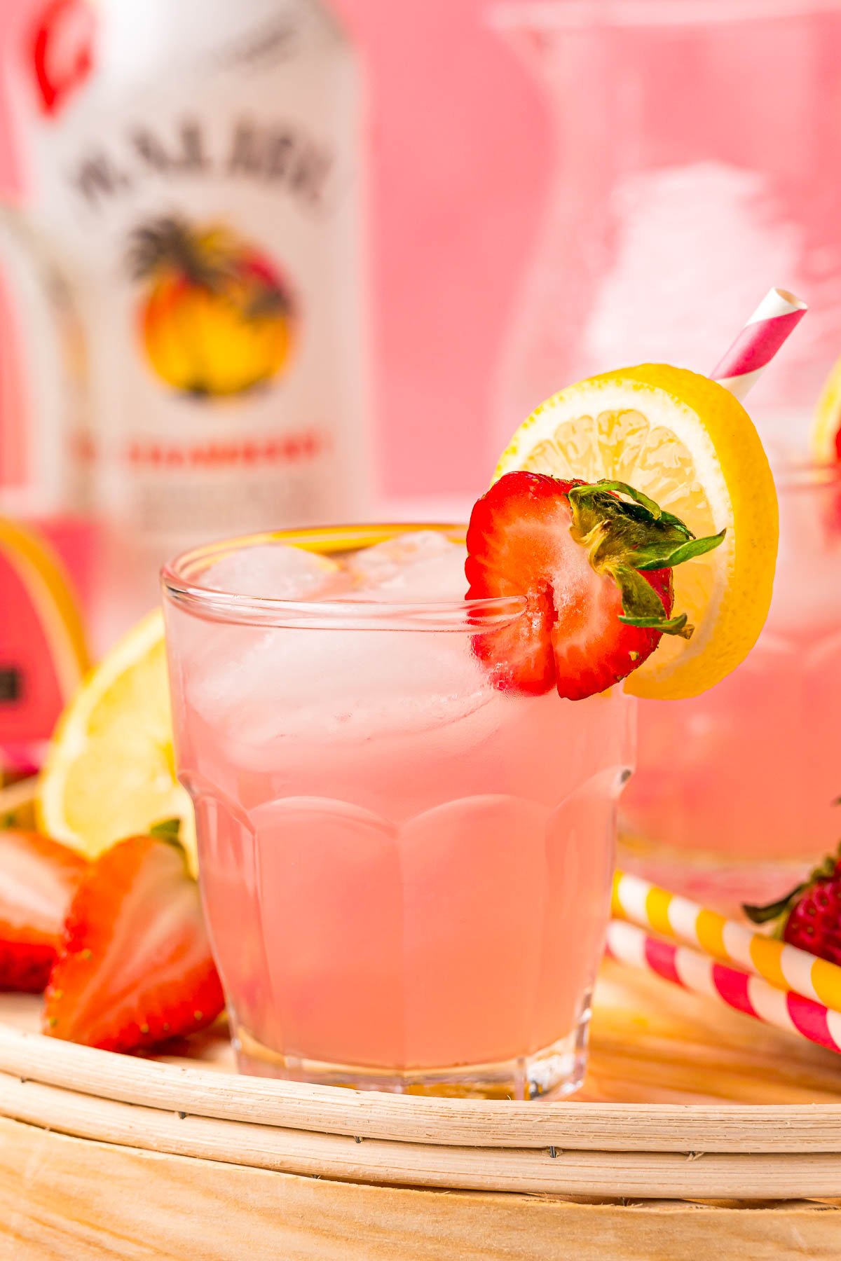 Close up photo of a small glass filled with a pink lemonade vodka cocktail on a rattan tray.