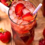 Close up photo of a glass of strawberry sweet tea on a wooden board with strawberries scattered around.