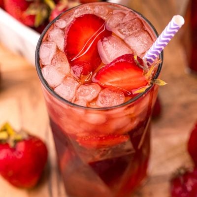 Close up photo of a glass of strawberry sweet tea on a wooden board with strawberries scattered around.