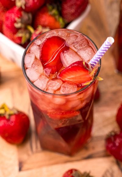 Close up photo of a glass of strawberry sweet tea on a wooden board with strawberries scattered around.