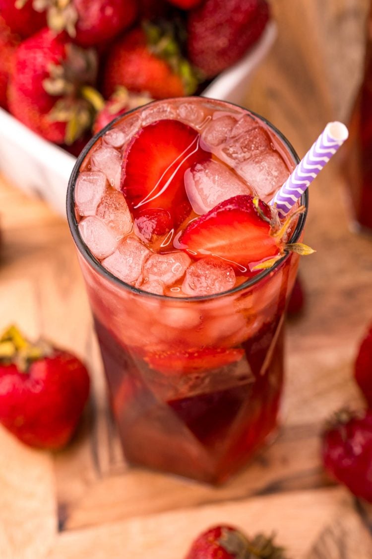 Close up photo of a glass of strawberry sweet tea on a wooden board with strawberries scattered around.