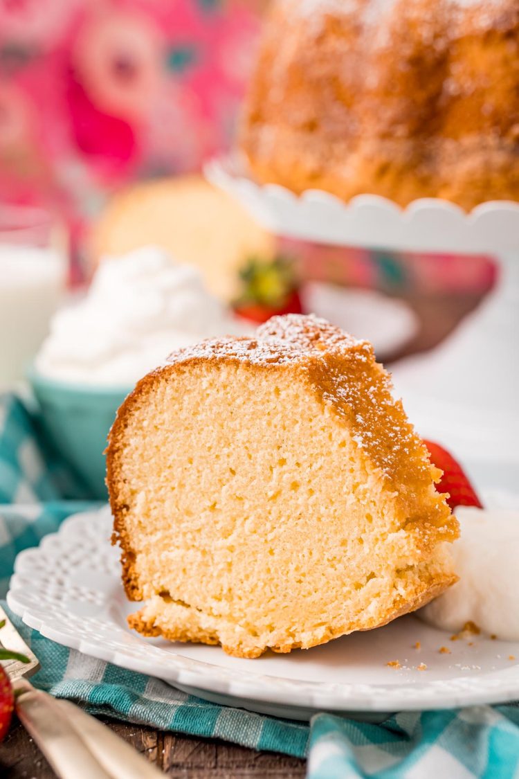 Close up photo of a slice of whipping cream cake on a white plate with whipped cream and a strawberry on the side.