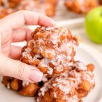 Close up photo of a woman's hand holding an apple fritter.