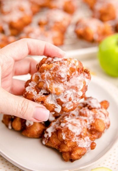 Close up photo of a woman's hand holding an apple fritter.