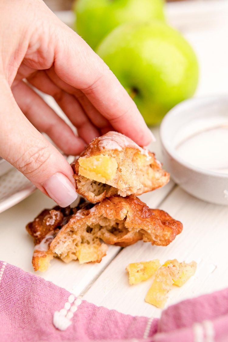A woman's hand holding a piece of apple fritter that's been broken off to show the inside texture.