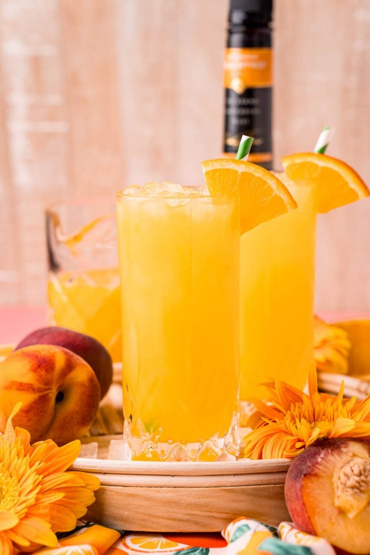 Close up photo of a glass filled with a fuzzy navel cocktail on a wooden serving tray.