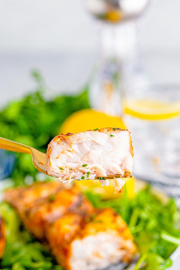 A fork holding a bite of mahi mahi fish above a plate.