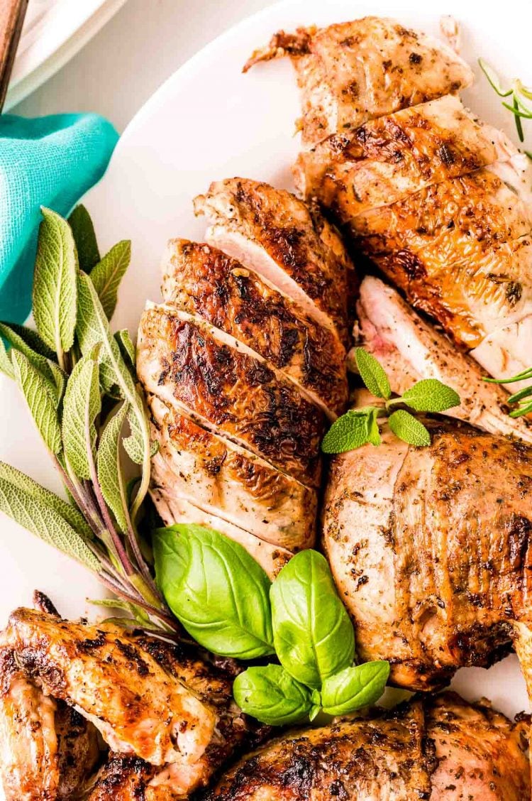 Grilled Italian chicken on a white plate with herbs.