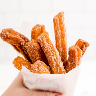 A woman's hand holding churros wrapped in parchment paper.