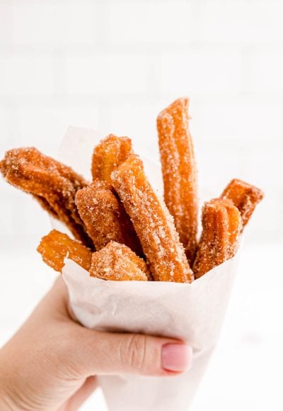 A woman's hand holding churros wrapped in parchment paper.