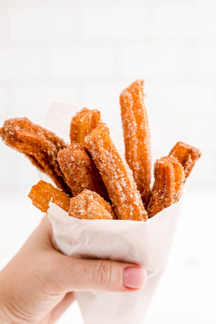 A woman's hand holding churros wrapped in parchment paper.