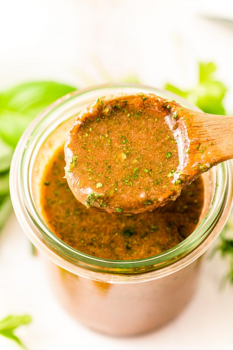 Close up photo of a wooden spoon scooping italian grilled chicken marinade out of a wide mouth glass jar.