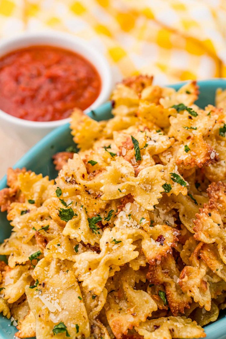 Close up photo of Pasta chips in a teal bowl with marinara sauce to the side.