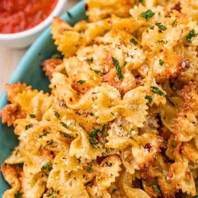 Close up photo of Pasta chips in a teal bowl with marinara sauce to the side.