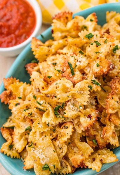 Close up photo of Pasta chips in a teal bowl with marinara sauce to the side.