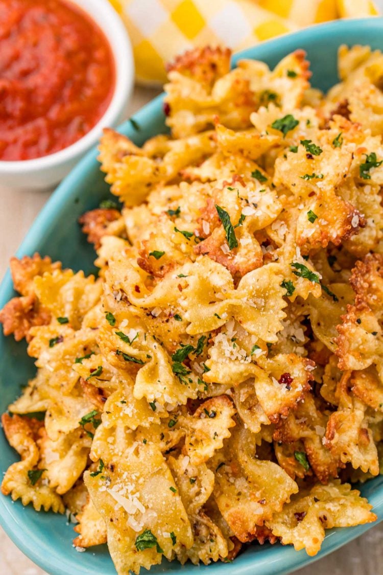 Close up photo of Pasta chips in a teal bowl with marinara sauce to the side.