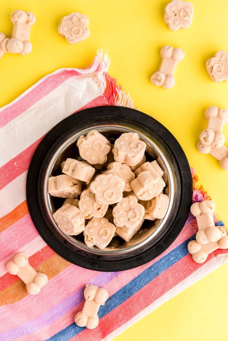 Overhead photo of frozen dog treats in a dog bowl on a colorful napkin.