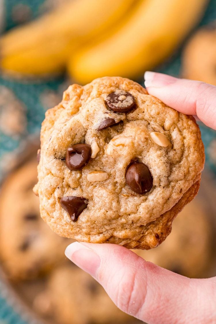 A woman's hand holding a banana bread cookie close to the camera.