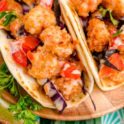 Close up photo of bang bang shrimp tacos on a wooden plate.