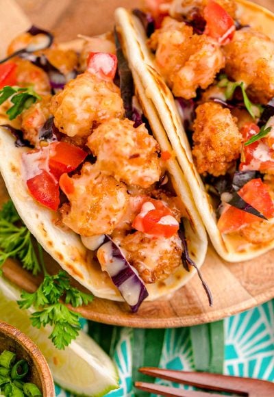 Close up photo of bang bang shrimp tacos on a wooden plate.