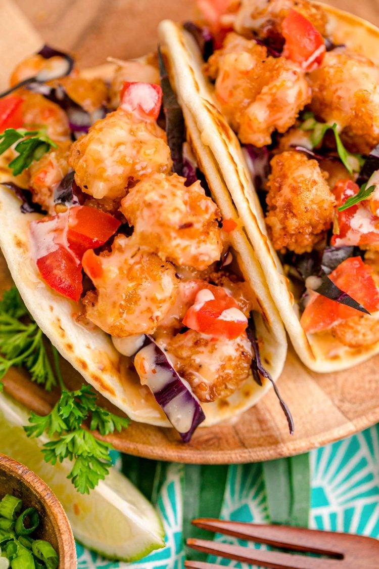 Close up photo of bang bang shrimp tacos on a wooden plate.