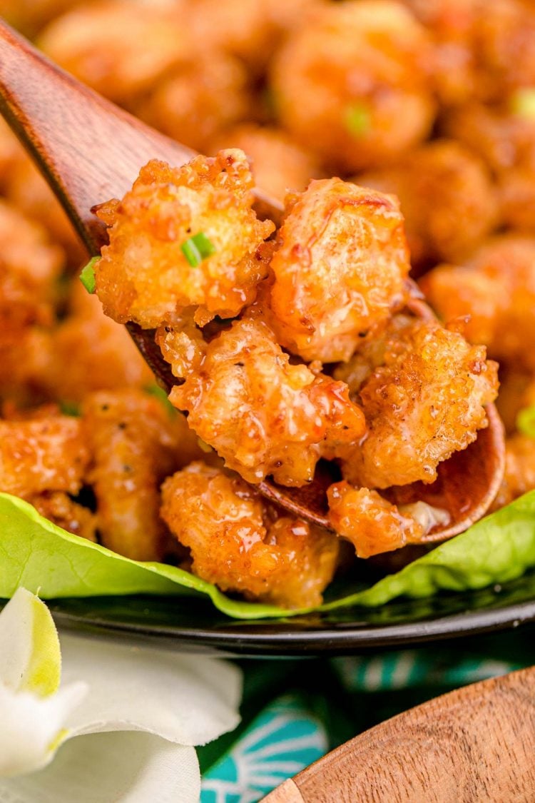 Bang Bang shrimp being scooped off a plate with a wooden spoon.
