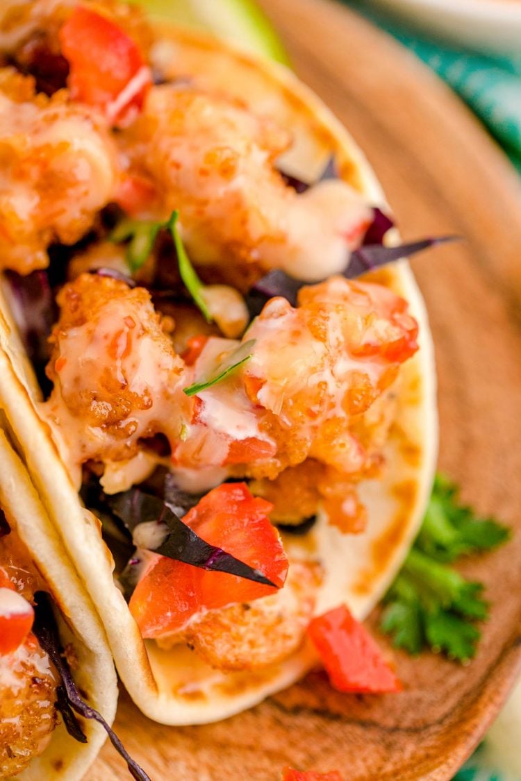 Close up photo of bang bang shrimp tacos on a wooden plate.