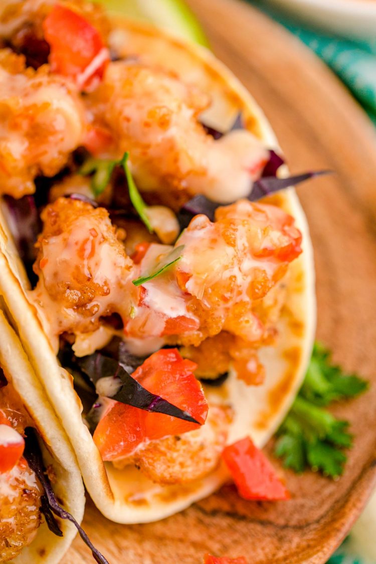 Close up photo of bang bang shrimp tacos on a wooden plate.