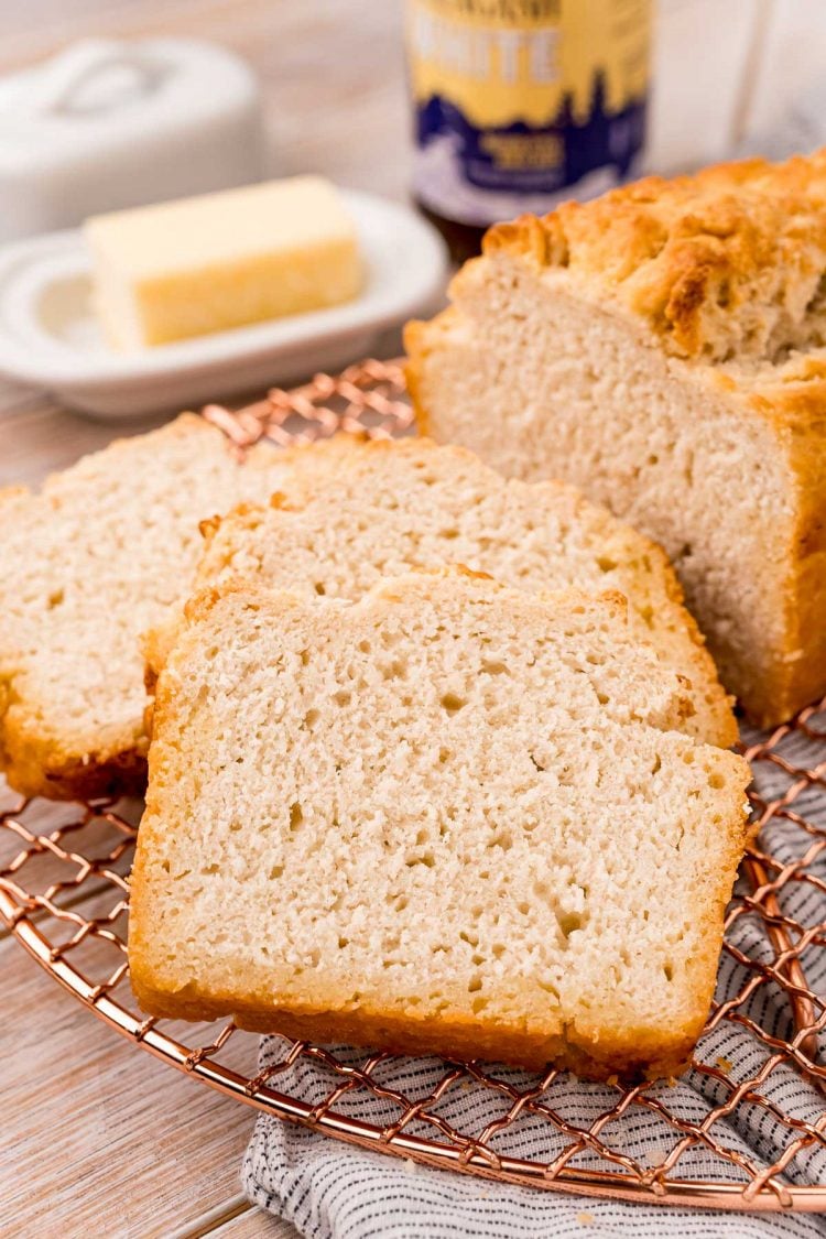 Close up photo of a loaf of beer bread with slices on a wire rack.