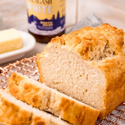 A loaf of beer bread on a copper wire rack that has been sliced.