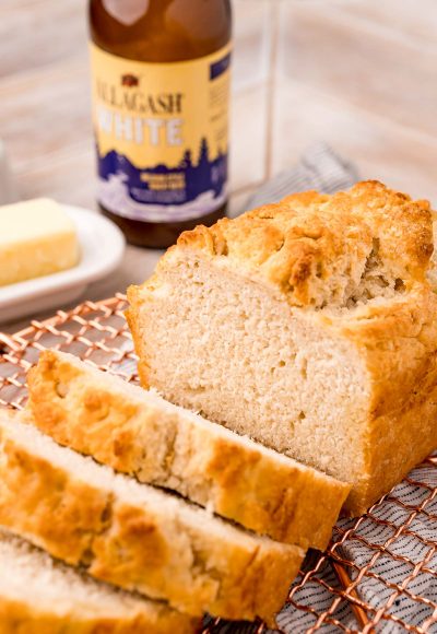 A loaf of beer bread on a copper wire rack that has been sliced.