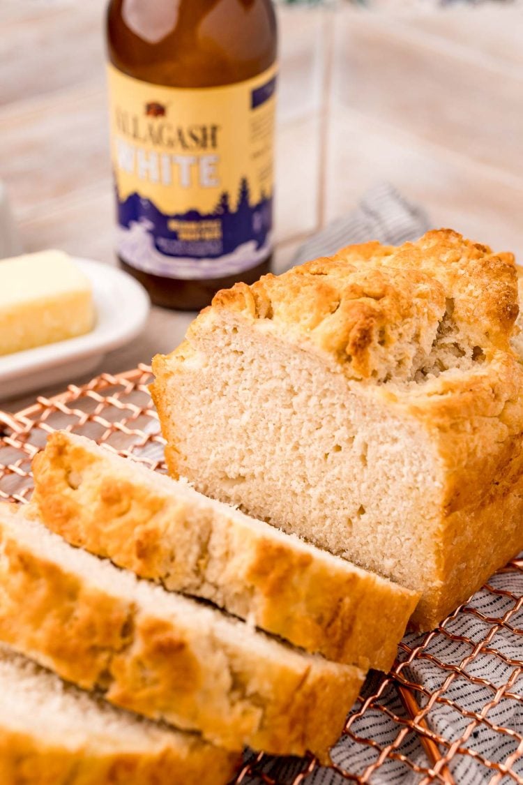 A loaf of beer bread on a copper wire rack that has been sliced.