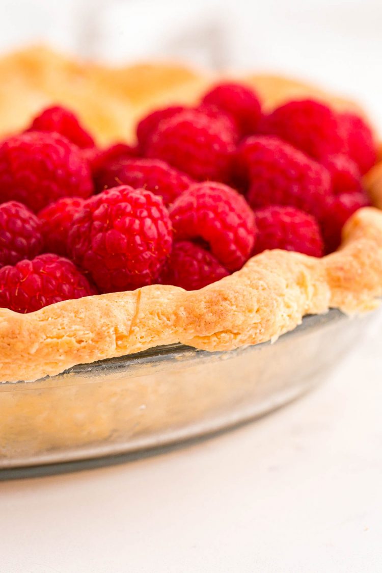 Fresh raspberries sitting in a cream cheese pie crust in a glass pie dish.