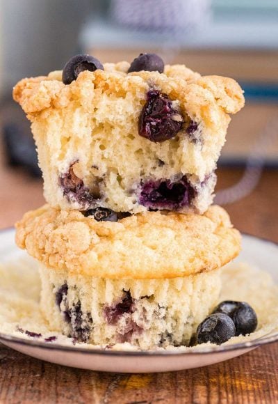 Close up photo of two sourdough blueberry muffins stacked on top of each other on a white plate. The top muffin is missing a bite.