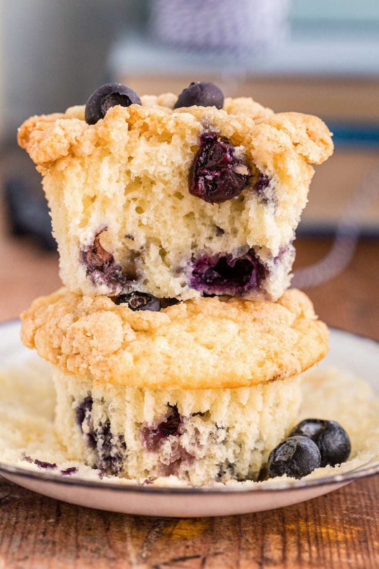 Close up photo of two sourdough blueberry muffins stacked on top of each other on a white plate. The top muffin is missing a bite.