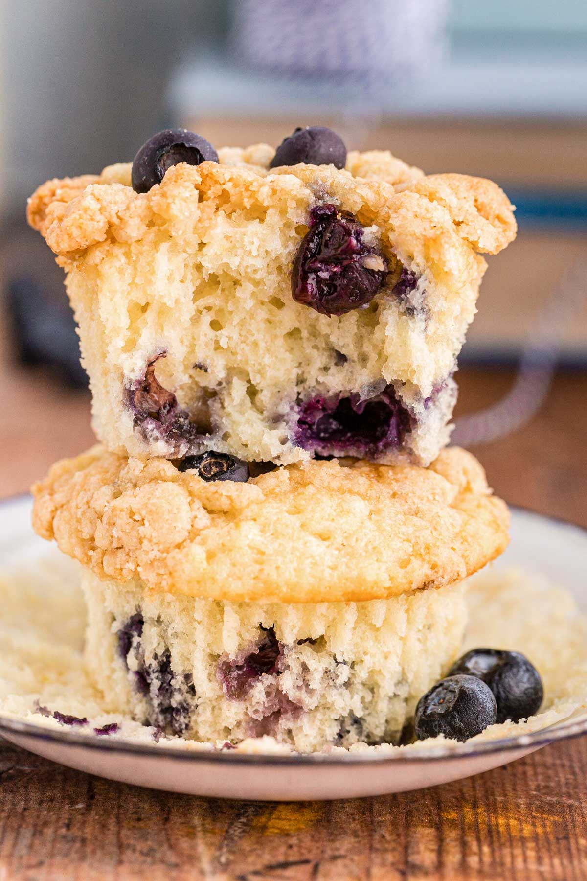 Close up photo of two sourdough blueberry muffins stacked on top of each other on a white plate. The top muffin is missing a bite.