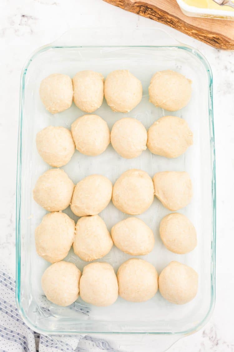 Balls of dough for dinner rolls in a glass baking pan.