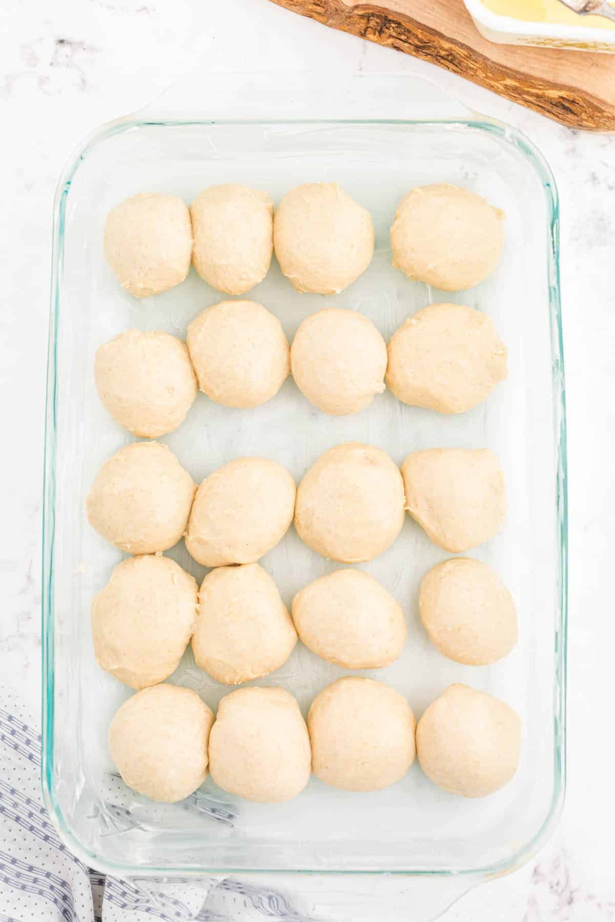 Balls of dough for dinner rolls in a glass baking pan.